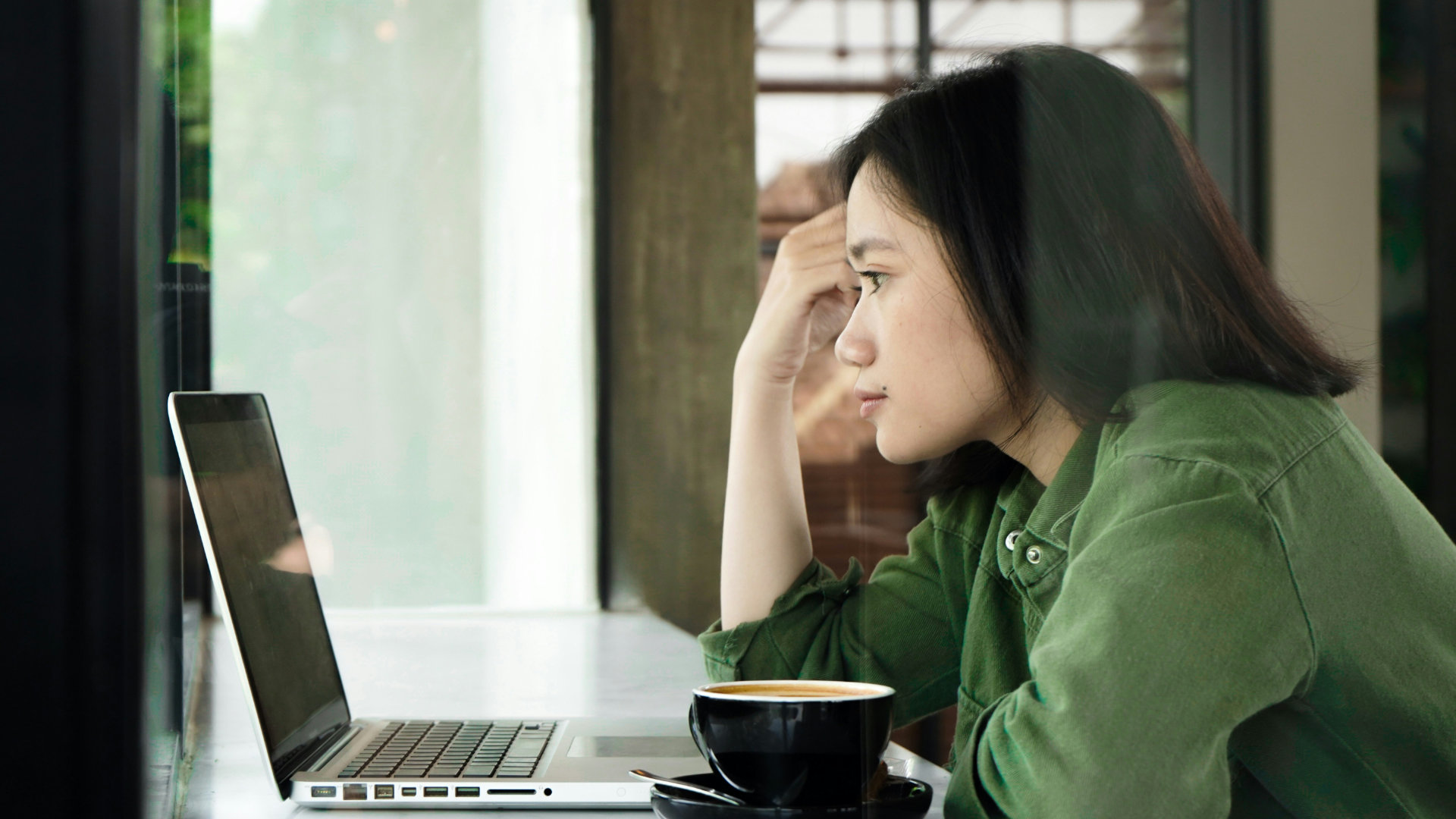 A person searching on a laptop with a cup of coffee, thoughtful and focused