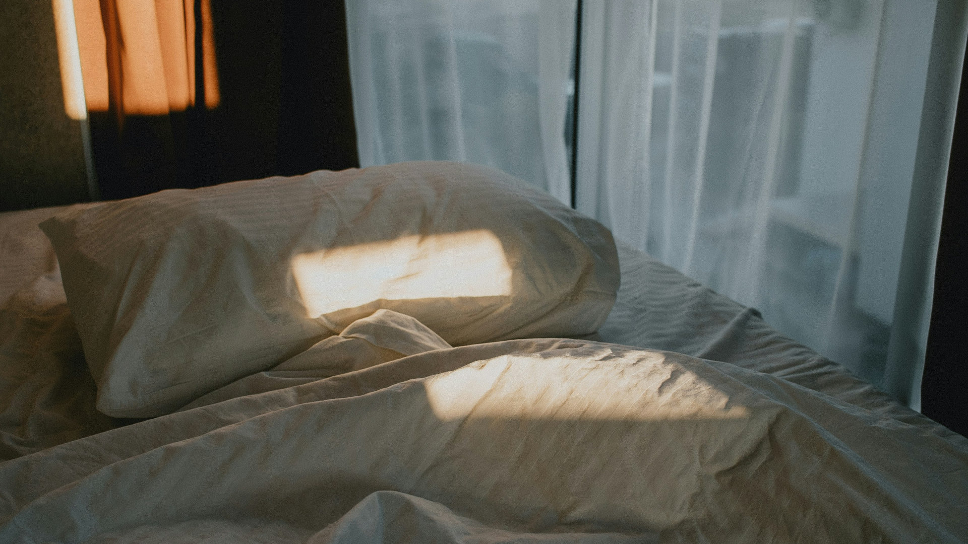 A peaceful bedroom scene with soft linens and morning light through sheer curtains